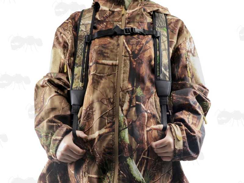 Black Canvas and Tree Camouflage Neoprene Backpack Harness Style Rifle Sling Shown Being Worn Over a Padded Camouflage Jacket, with Thumbs in The Thumb-Loops